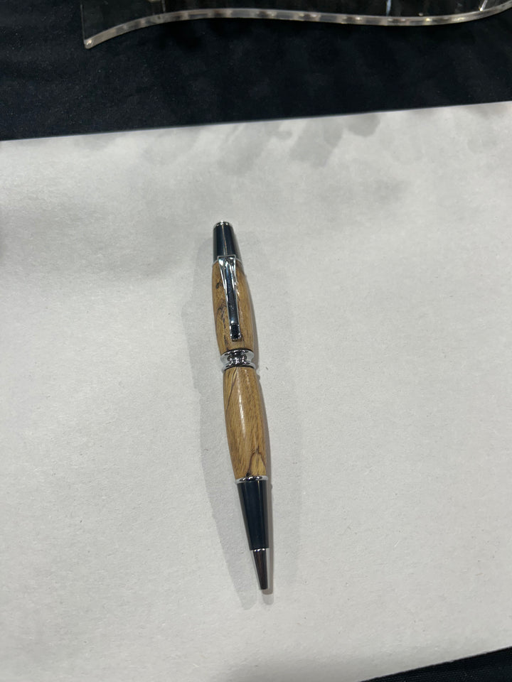 Ball point pen with a Silver metal and black hardware with black last diamond. And a in pecan wood . friction finish.