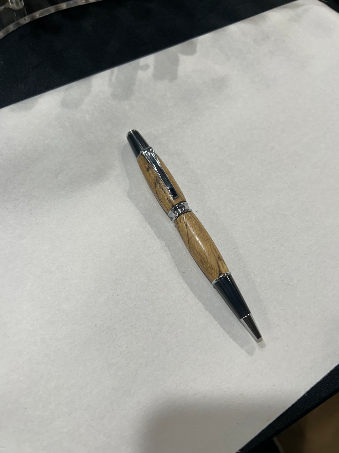 Ball point pen with a Silver metal and black hardware with black last diamond. And a in pecan wood . friction finish.